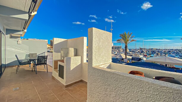 A terrace with a table and chairs, a view of a marina with boats, and a palm tree. - Intemporal Duplex Marina T2 Hsrentals Vilamoura (Loulé)