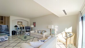 A living room with a glass coffee table, a sofa, a TV, and a wicker chair. - Intemporal Duplex Marina T2 Hsrentals Vilamoura (Loulé)