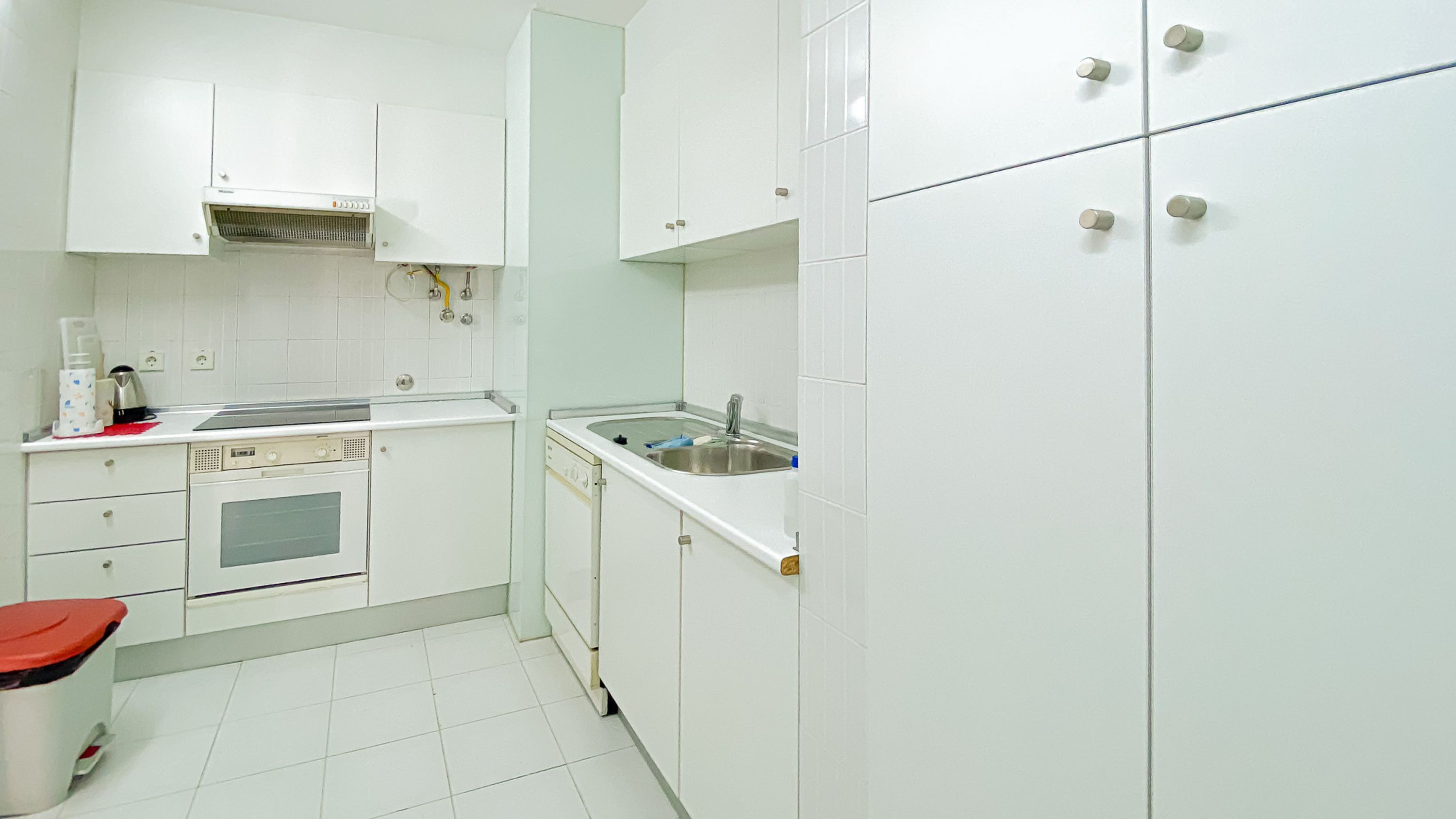A kitchen with white cabinets, a sink, a stove, and a trash bin.