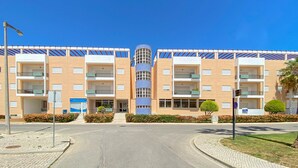 A modern building with multiple balconies, a central cylindrical structure, and a well-maintained garden area. - Marina Sol T3 Hsrentals Vilamoura (Loulé)