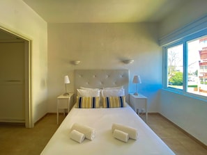 A hotel room with a large bed, two bedside lamps, a window with a view, and a door to the left.