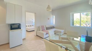 A modern living room with a glass dining table, white sofas, a microwave, and a ceiling light. - Yes Vilamoura Central - T1 Aldeia do Mar (Loulé)