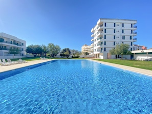 A swimming pool with a clear blue water surface, surrounded by a grassy area and trees.