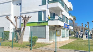 A white multi-story building with balconies, a green awning, and a sign indicating a business. - Yes Vilamoura Central - T1 Aldeia do Mar (Loulé)