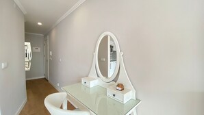 A modern bathroom with a glass vanity, a large oval mirror, and a white chair. - Est dio T nis Golf Mar Hsrentals Vilamoura (Loulé)