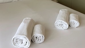 A neatly made bed with white linens and two rolled towels placed on the bed.