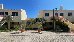 A courtyard with cobblestone flooring, potted plants, and buildings with balconies and windows.