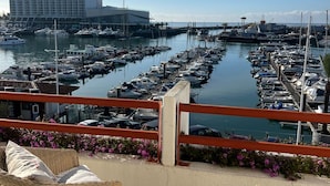Ein Yachthafen mit zahlreichen vertäuten Booten, ein Hotelgebäude im Hintergrund und Korbstühle auf einem Balkon mit Blick auf den Hafen.