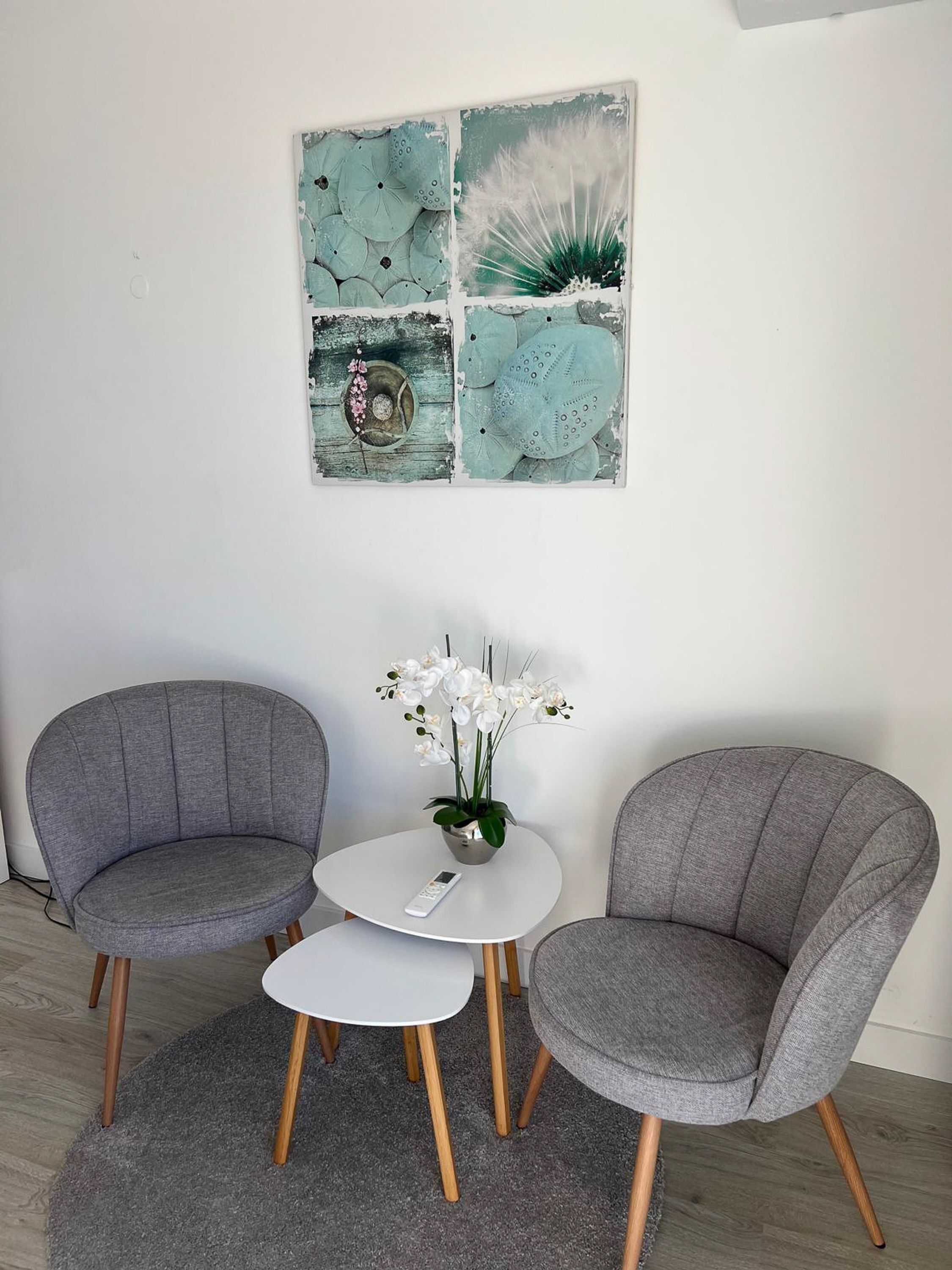 A room with two grey armchairs, a small white table, and a wall-mounted artwork featuring abstract designs.