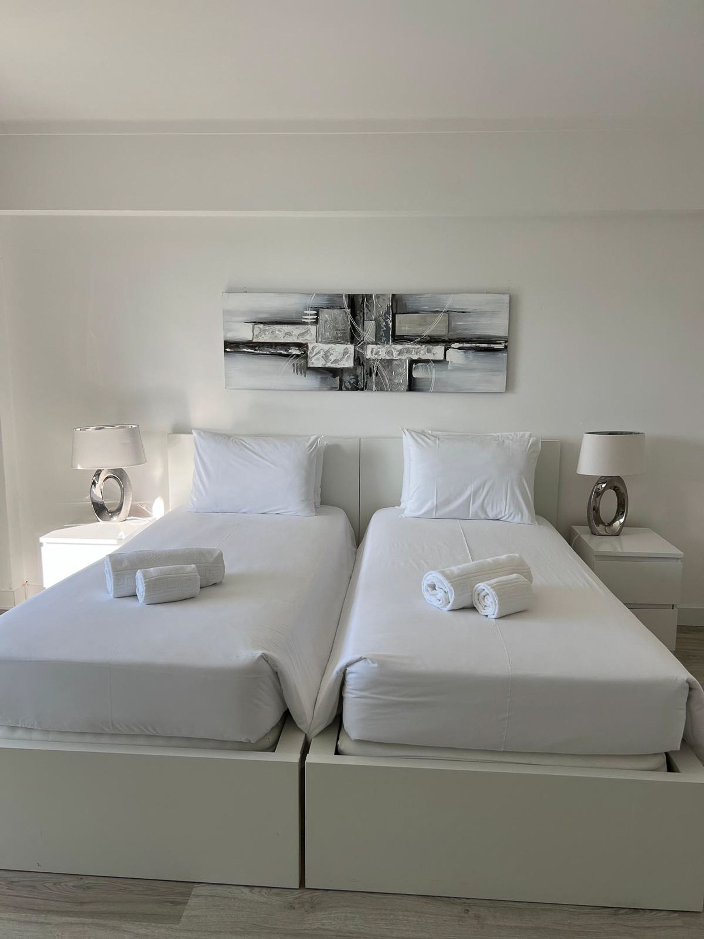 A double bed with white linens and towels, two bedside tables with lamps, and a modern abstract painting on the wall.