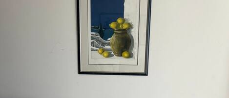 Une chambre à coucher avec un lit, un tableau encadré représentant des citrons et un vase, ainsi que des coussins à rayures.