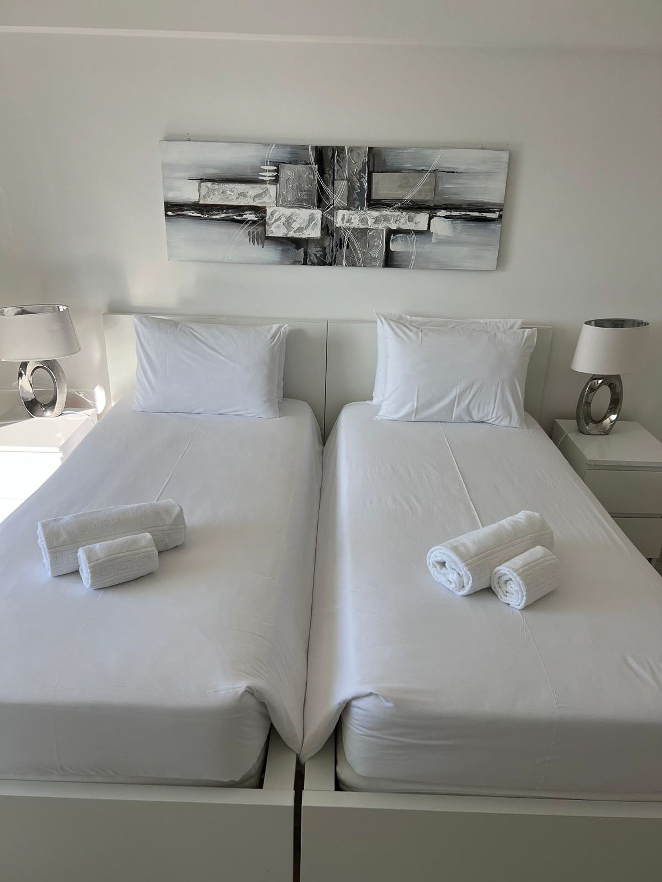 A hotel room with two beds, white linens, and towels. There is a modern abstract painting on the wall above the beds.