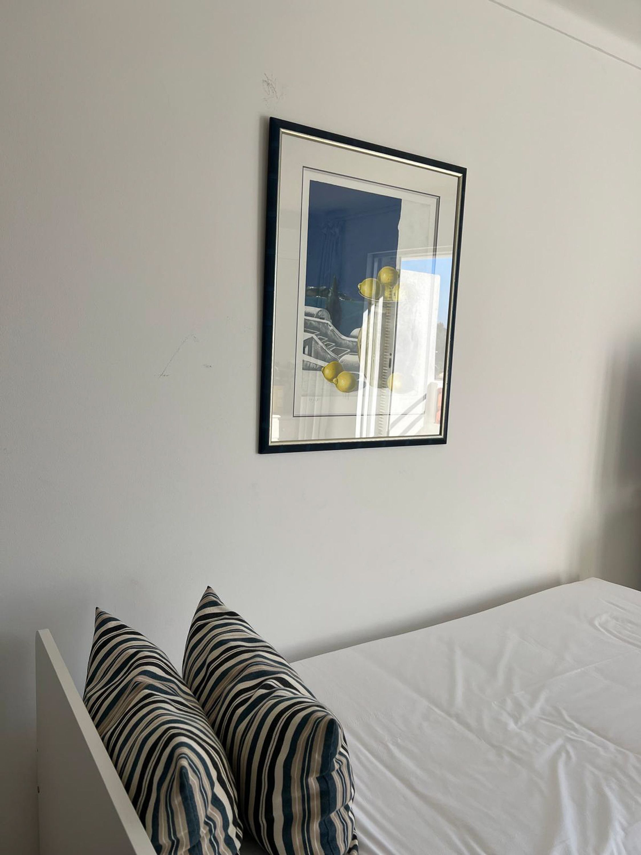 Un dormitorio con una cama blanca, dos almohadas a rayas y un cuadro en la pared.