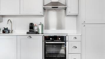 Eine moderne Küche mit weißen Schränken, einer Edelstahl-Dunstabzugshaube, einem eingebauten Backofen und einer Kaffeemaschine.