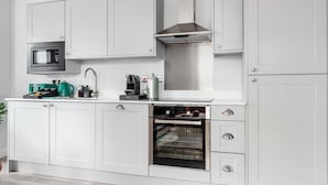 Una cocina moderna con armarios blancos, horno empotrado, microondas y campana extractora de acero inoxidable.