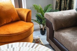 Una sala de estar con un sillón color mostaza, un sofá marrón y una planta en maceta.