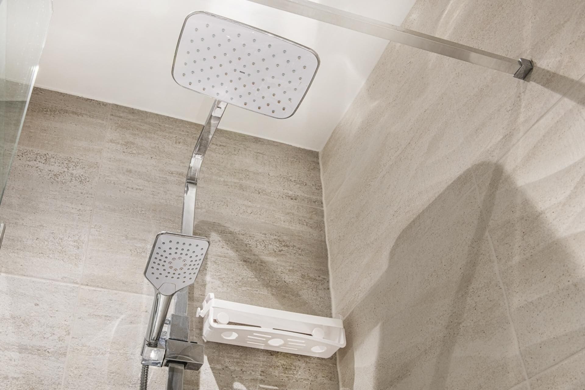 A shower area with a handheld showerhead and a wall-mounted showerhead, both with multiple nozzles.