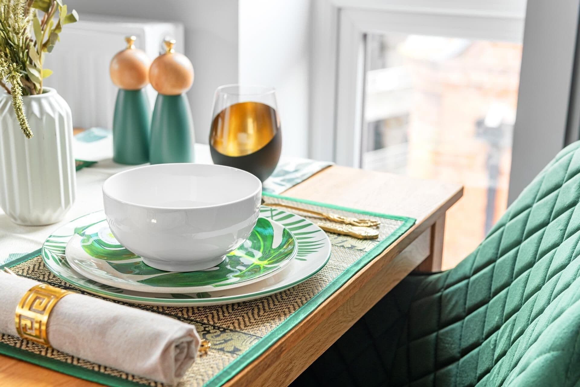 A dining table with a white bowl, green plates, and a gold-colored glass.