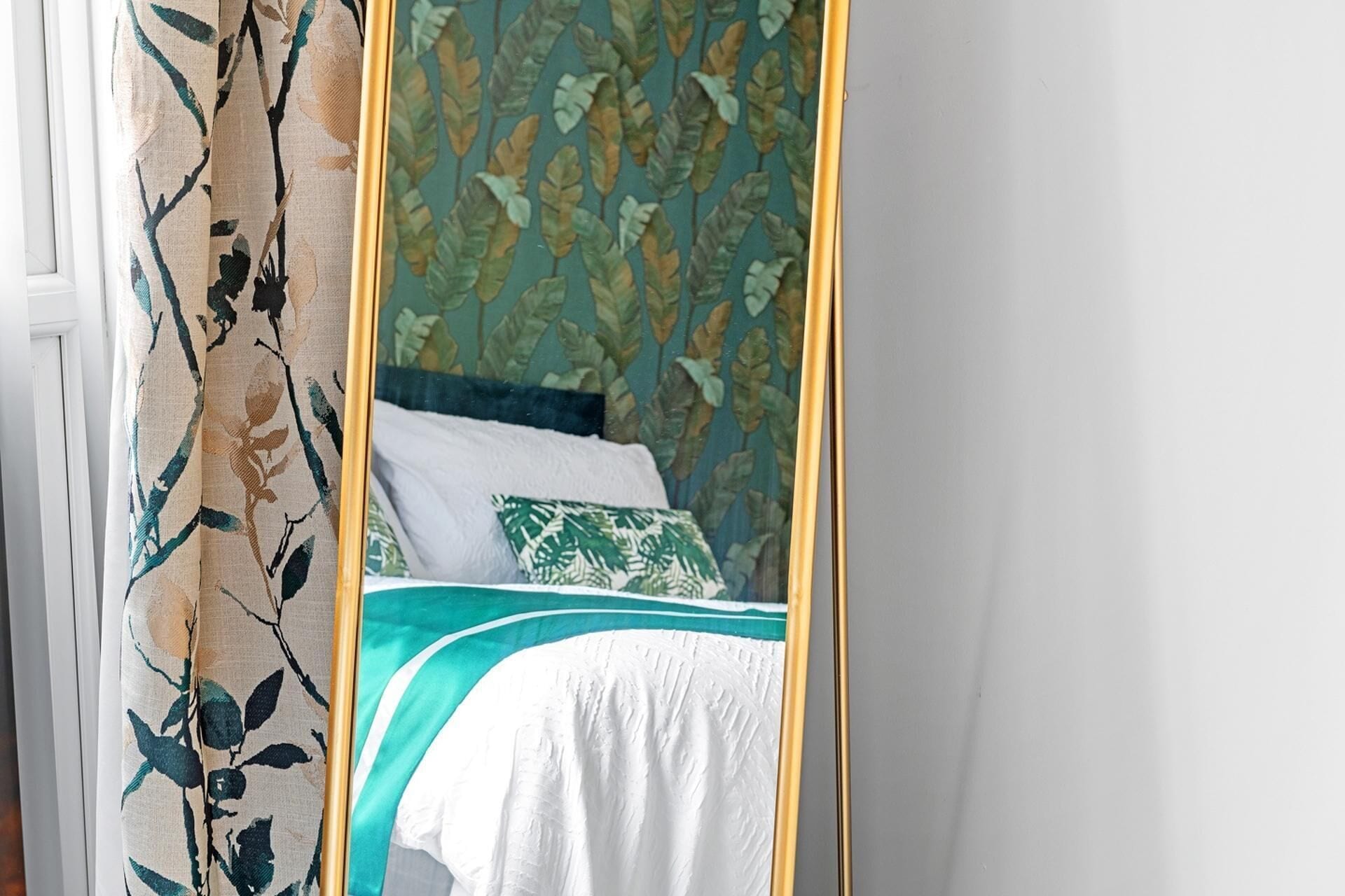 Une chambre à coucher avec un lit, un oreiller à motifs verts et blancs, et un rideau orné de motifs de feuilles.