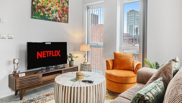 Una sala de estar moderna con un televisor de pantalla plana, una mesa redonda de centro, un sofá y un cuadro en la pared.