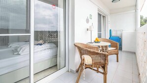 Uma varanda com uma cama, cadeiras de vime, uma mesa e vista do céu.