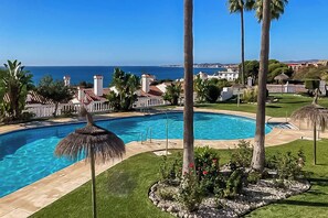 A swimming pool with a clear view of the ocean, surrounded by palm trees and a well-maintained lawn.