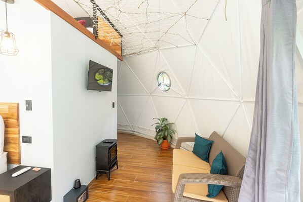 Una sala acogedora con piso de madera, un sofá con cojines verde agua, una mesita y una planta en maceta.