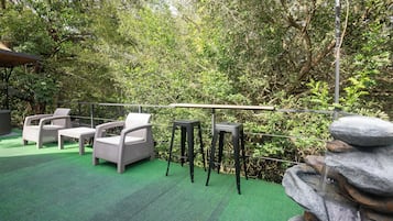 Un espacio al aire libre con sillas y mesas, rodeado de abundante follaje y una fuente de piedra.