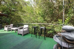 An outdoor seating area with chairs and tables, surrounded by lush greenery and a stone water feature. - Macas Moon Glamping (Sierra)