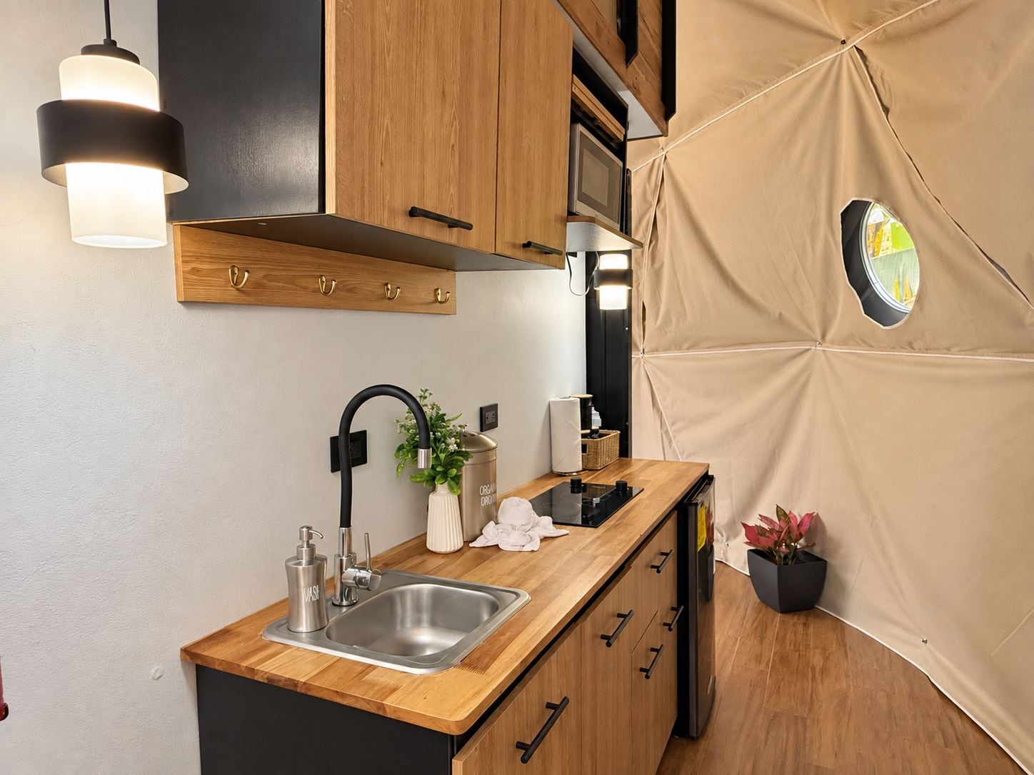 Cozinha compacta com bancada de madeira, pia de aço inoxidável, torneira preta e luminária pendente.