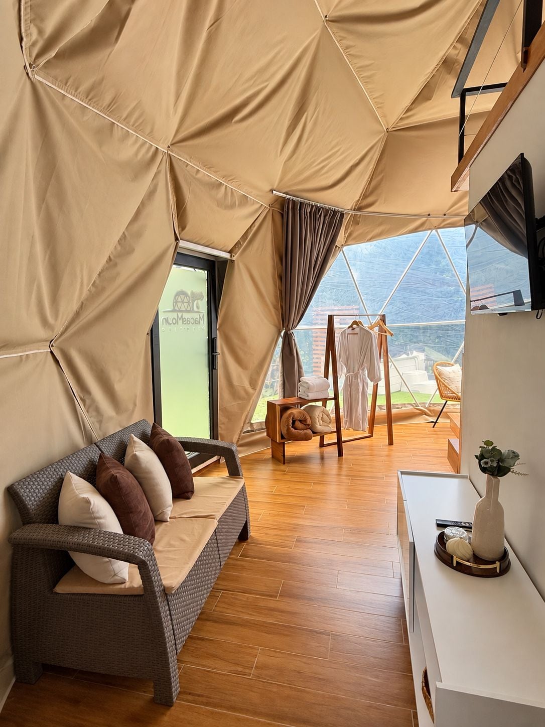 A tented room with a sofa, a wooden floor, a clothing rack, and a desk with a vase.