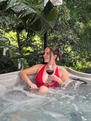A person in a red swimsuit sitting in a hot tub surrounded by lush greenery. - Macas Moon Glamping (Sierra)