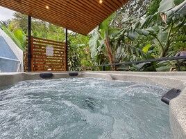 A hot tub area with a wooden roof, surrounded by lush greenery and banana plants.
