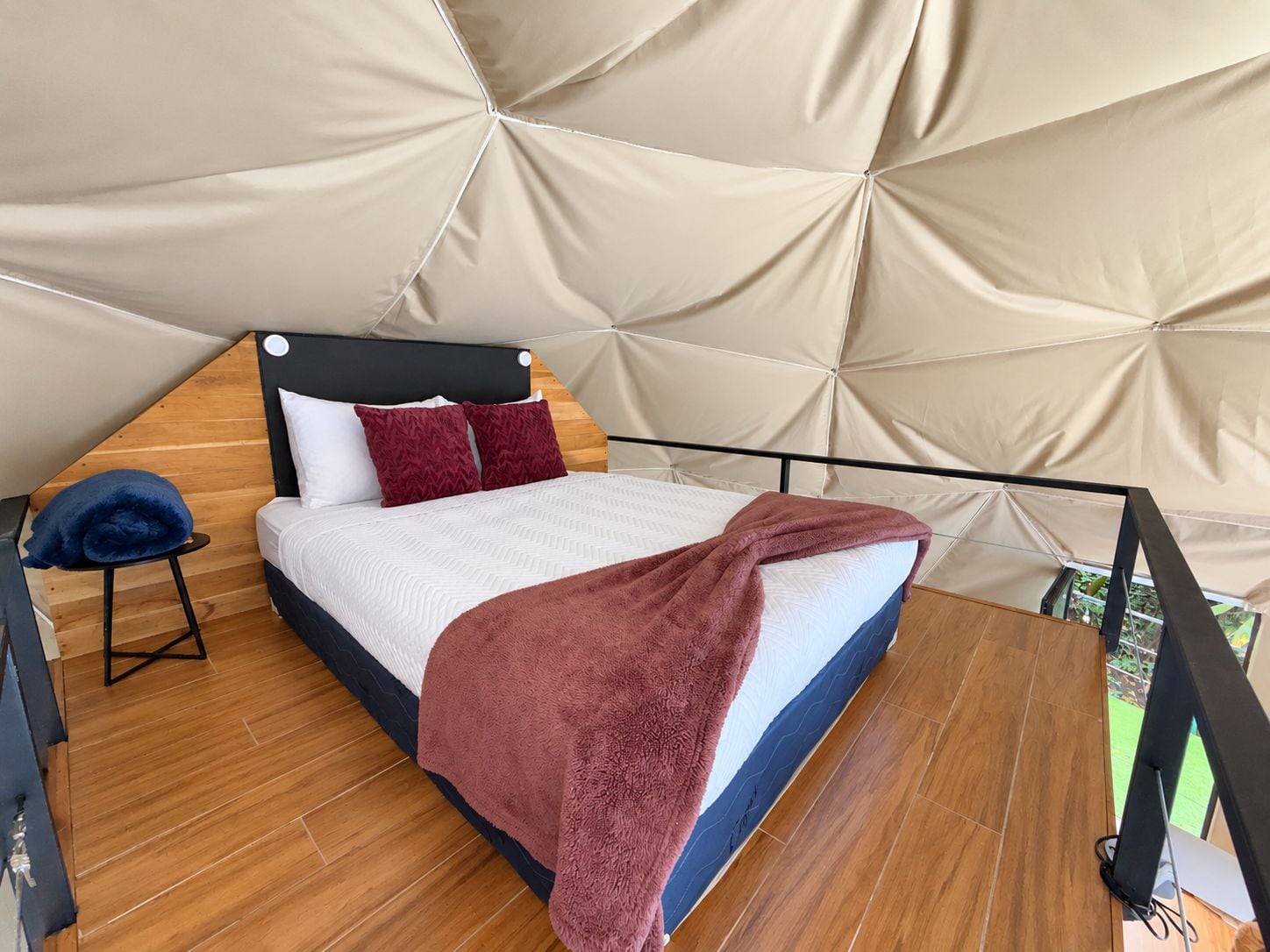 Een tentachtige kamer met een bed, een klein krukje en uitzicht op de natuur.