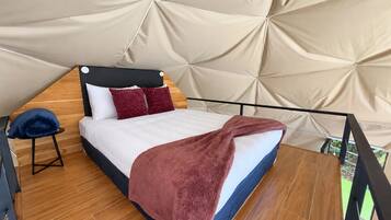 Een tentachtige kamer met een bed, een klein krukje en uitzicht op de natuur.