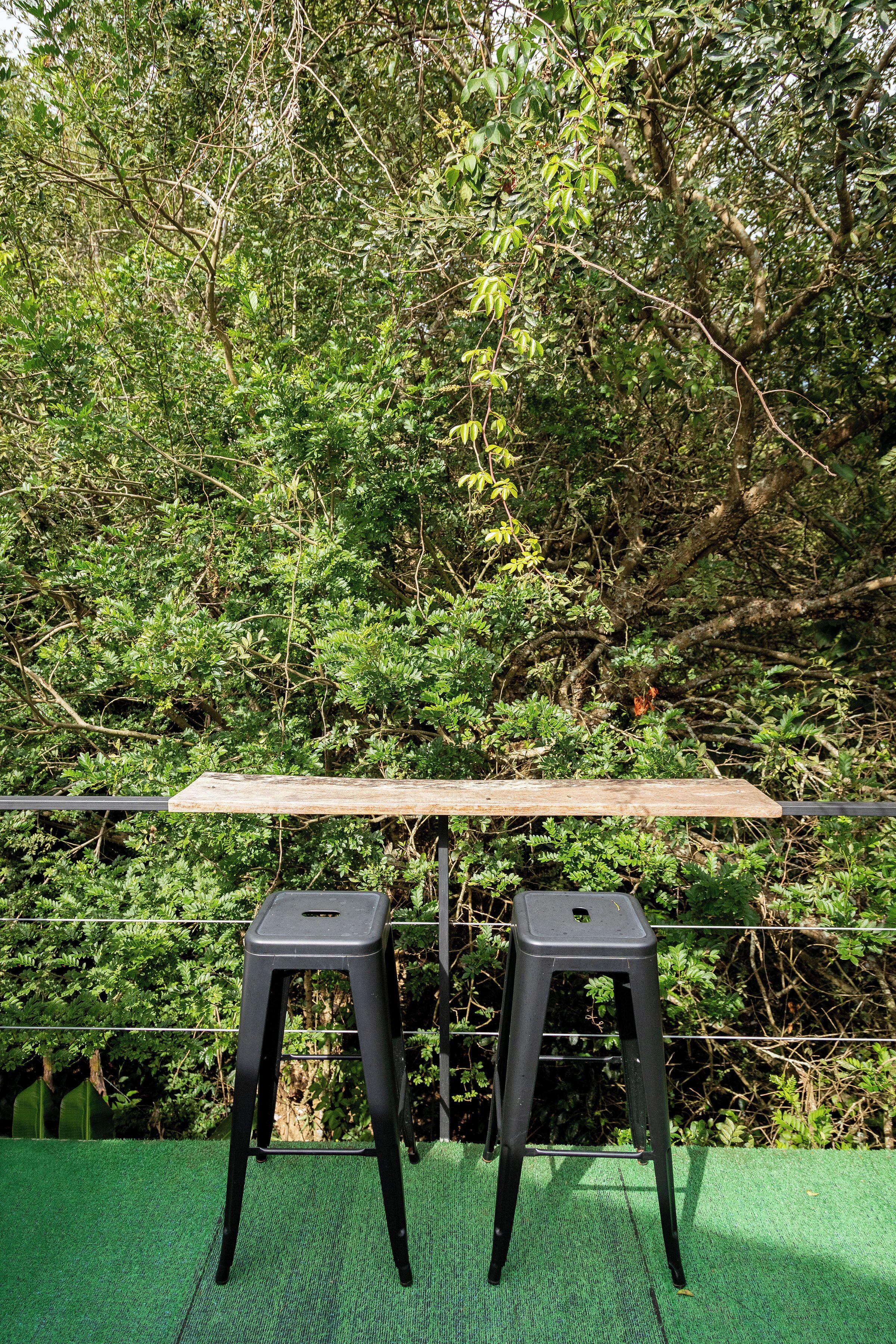 Dos taburetes de plástico negro sobre una superficie de césped artificial verde, con una mesa de madera delante.