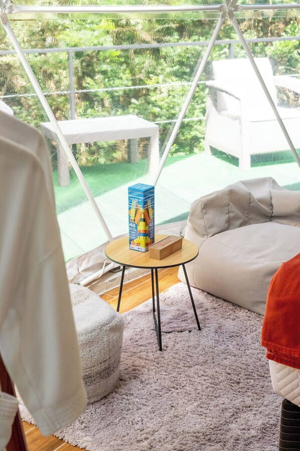 A cozy room with a view of greenery, a small round table with a box, a white couch, and a fluffy rug. - Macas Moon Glamping (Sierra)
