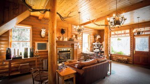 A log cabin interior with a fireplace, wooden furniture, antlers on the ceiling, and a cozy fireplace area. - Rustic Lake Louise Cabin | Fireplace & Balcony (Lake Louise)