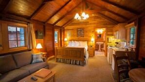 A log cabin interior with a wooden ceiling, a central bed, a sofa, a dining table, and a kitchen area. - Rustic Lake Louise Cabin | Fireplace & Balcony (Lake Louise)