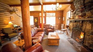L’intérieur d’une cabane en rondins, avec une cheminée en pierre, des canapés en cuir, des meubles en bois et un lustre.