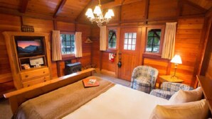 Une pièce chaleureuse, aménagée dans un chalet en bois, comprenant un lit, un téléviseur, un bureau et une chaise.