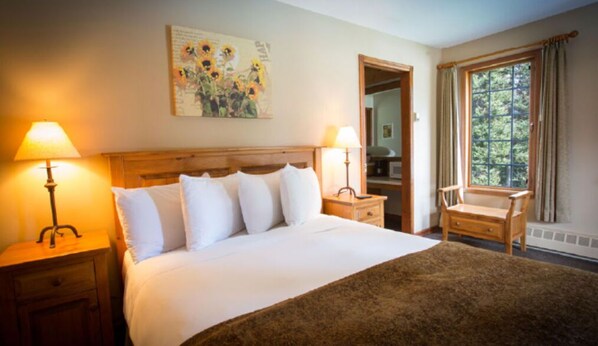 A hotel room with a large bed, two bedside tables with lamps, a chair, a window with curtains, and a painting on the wall.