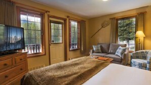 Una habitación de hotel con cama, sofá, televisor y ventanas grandes con cortinas.