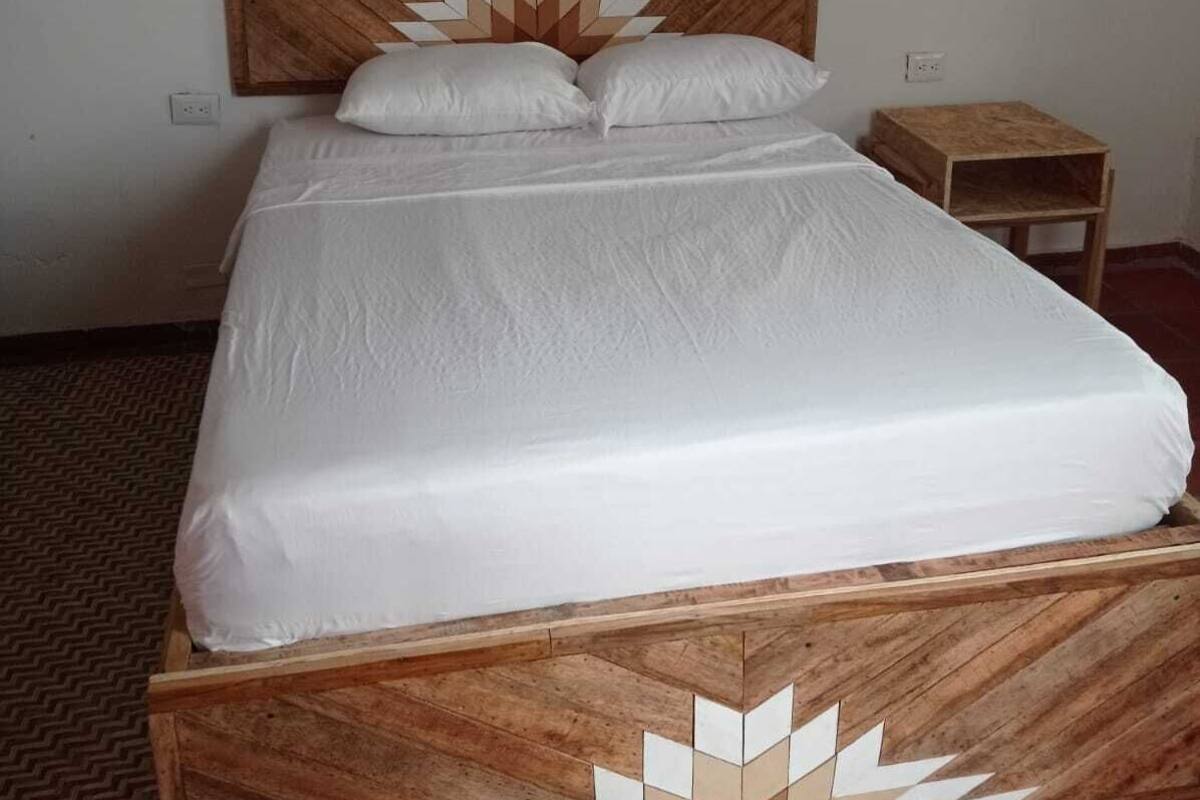Una cama con cabecera de madera y un estampado geométrico, una mesita de noche pequeña y suelo de baldosas.