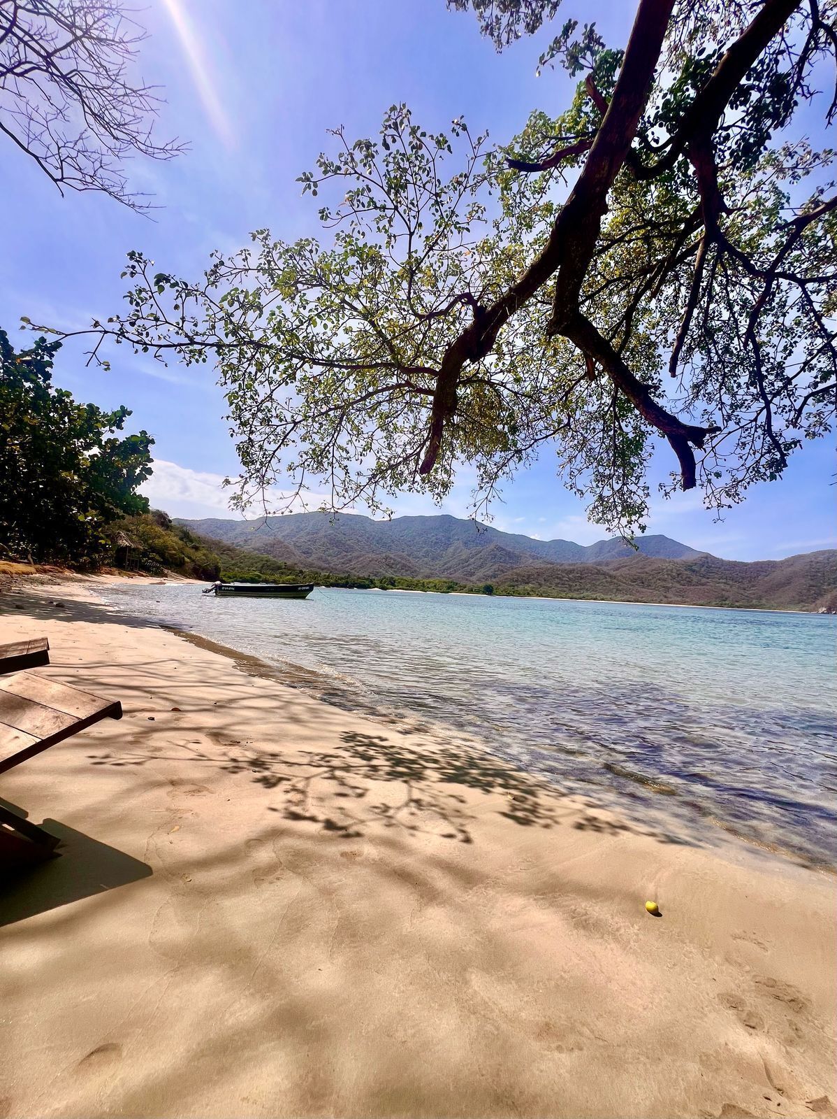 A beach with clear water, a boat, and mountains in the background.