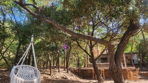 A rustic outdoor setting with a white macrame swing, wooden chairs, and a stone wall. - MISTICA Tayrona Cinto (Santa Marta)