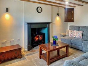 A cozy living room with a fireplace, a sofa, a wooden table, and a clock on the wall.