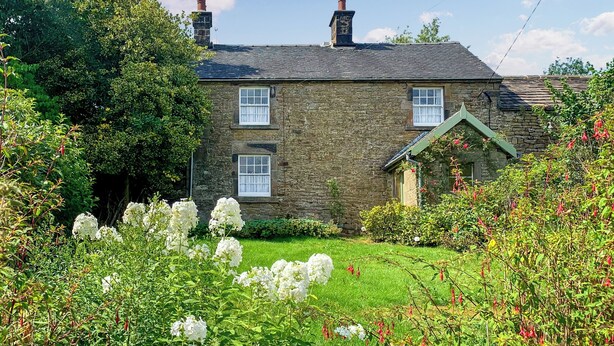 A stone house with a green roof, a small garden with white flowers, and a clear blue sky. - 3 bedroom accommodation in Leek (Leek)
