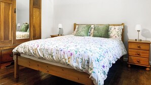 A bedroom with a wooden bed, floral bedding, a wooden wardrobe, and two bedside tables with lamps. - 3 bedroom accommodation in Leek (Leek)