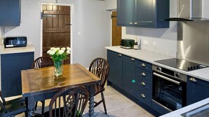 A modern kitchen with dark cabinets, a wooden dining table, and a vase of white flowers. - 3 bedroom accommodation in Leek (Leek)